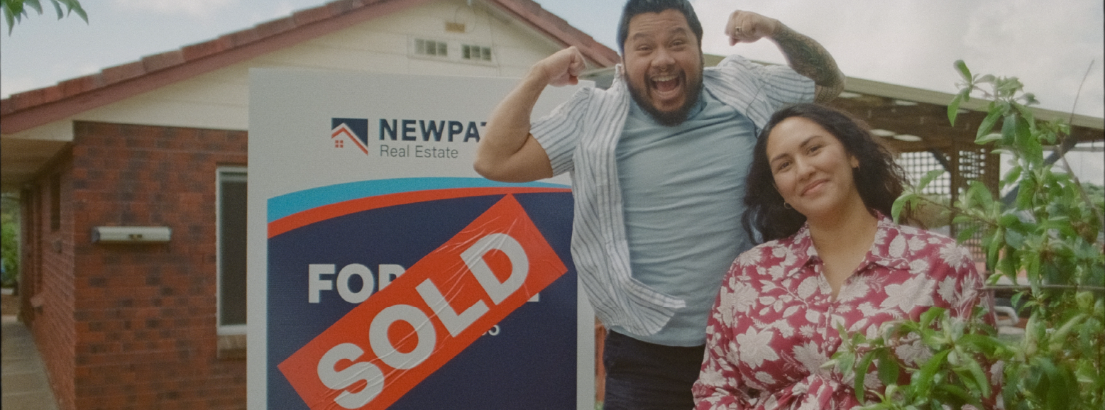 Couple standing out the front of a sold sign